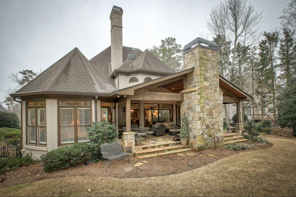 Covered stone patio with outdoor fireplace and seating area by Norm Hughes Homes.