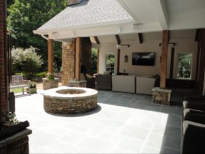 Stone patio with circular fire pit and covered seating area by Norm Hughes Homes.