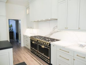  Professional-grade black and gold gas range in a bright white custom kitchen. image description: A stunning high-capacity range with gold accents serves as the focal point in this white kitchen renovation, highlighted by a full-height marble backsplash. 