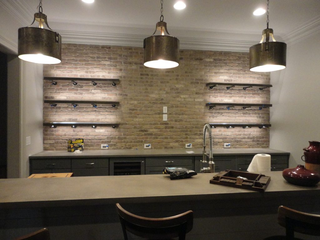 Alt Text: Industrial basement remodel ideas featuring a brick accent wall and rustic bar lighting.