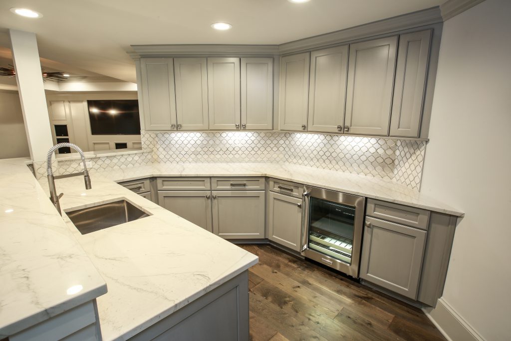 Basement remodel in-law suite featuring a modern gray and white kitchenette with a beverage fridge.
