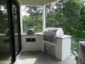 Covered patio outdoor kitchen at a luxury lake house featuring a built-in stainless steel grill and ceramic smoker.