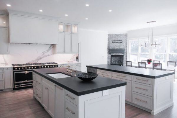 Luxury white custom kitchen featuring a large double island with dark countertops and modern gold hardware.