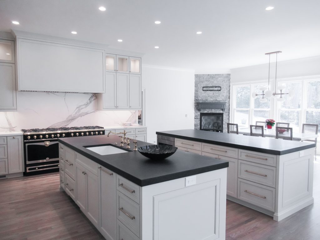 Luxury white custom kitchen featuring a large double island with dark countertops and modern gold hardware.