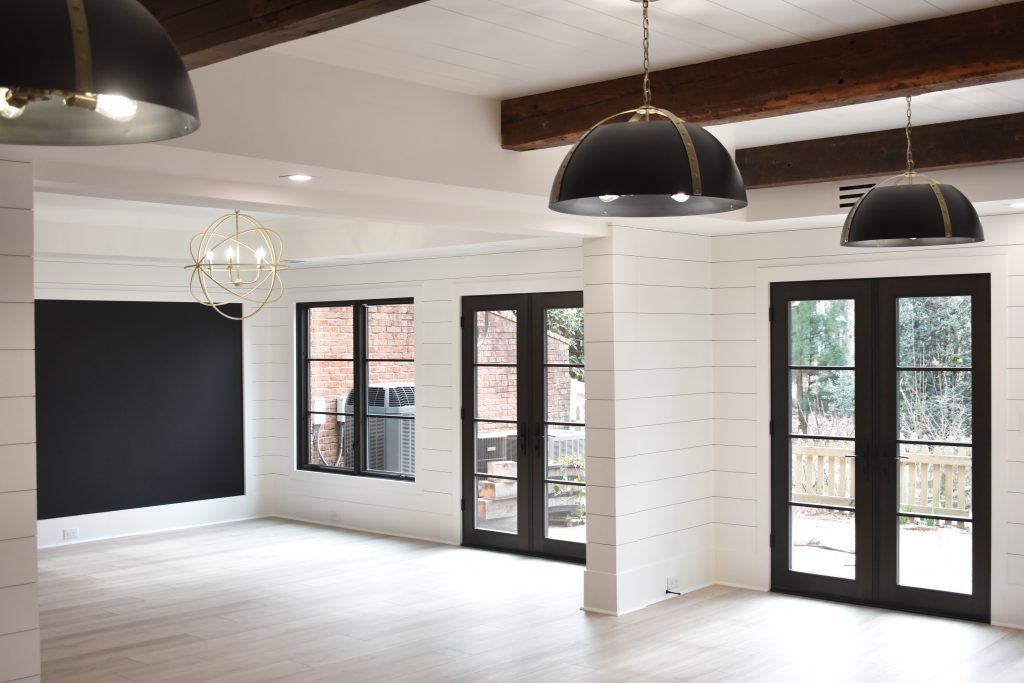 Bright open-concept home interior with white shiplap walls, dark double French doors, and industrial pendant lights.
